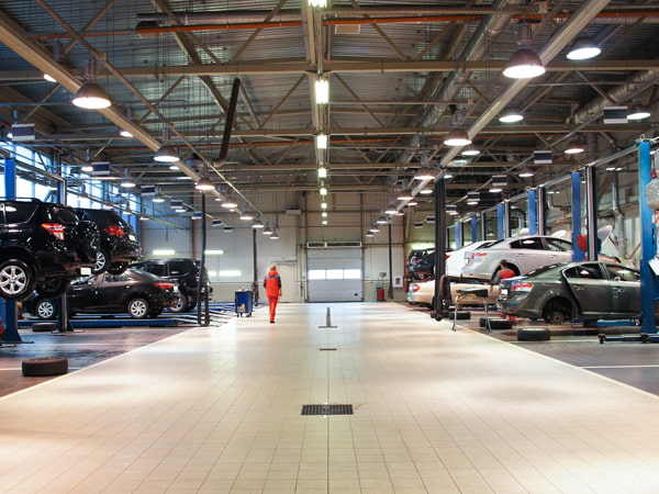 A large auto shop is shown with service bays on on both sides of a tiled center aisleway, with LED lights illuminating the workspace from above