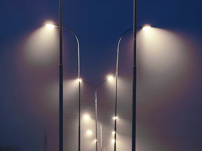 Cobra style LED street lights are shown illuminating the roadway below with fog in the night.
